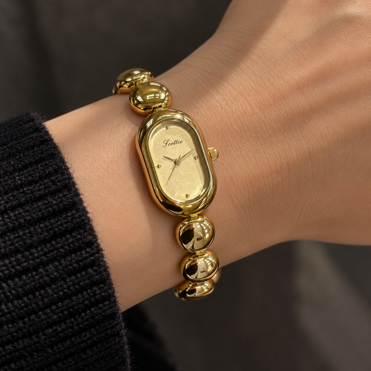 Scottie Champagne watch worn beside a black knit sleeve